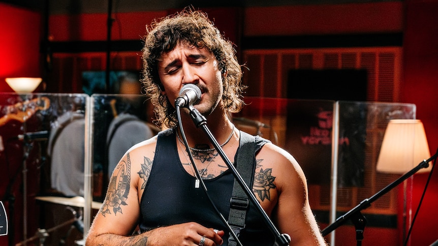 Person singing into a microphone while wearing a black singlet in the Like A Version studio