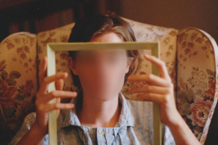A woman sits in an armchair holding an empty photo frame.