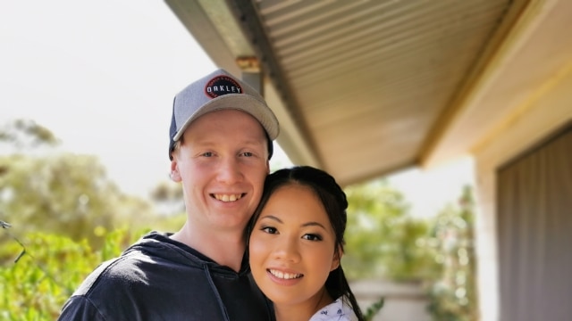 A man and a woman with her makeup done stand on a balcony hugging each other.