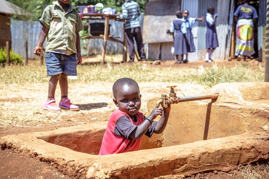 A boy crouches under a new tap at a school in Kenya.