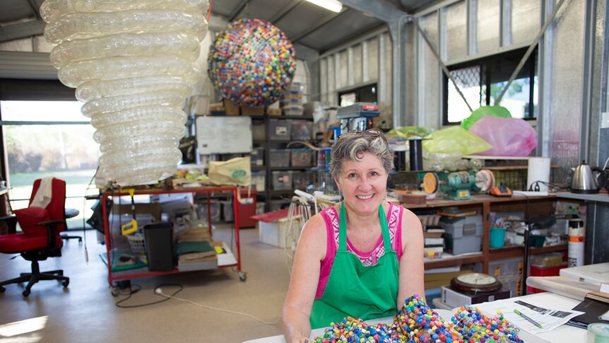 Woman sits with artwork of lots of plastic bottle tops.