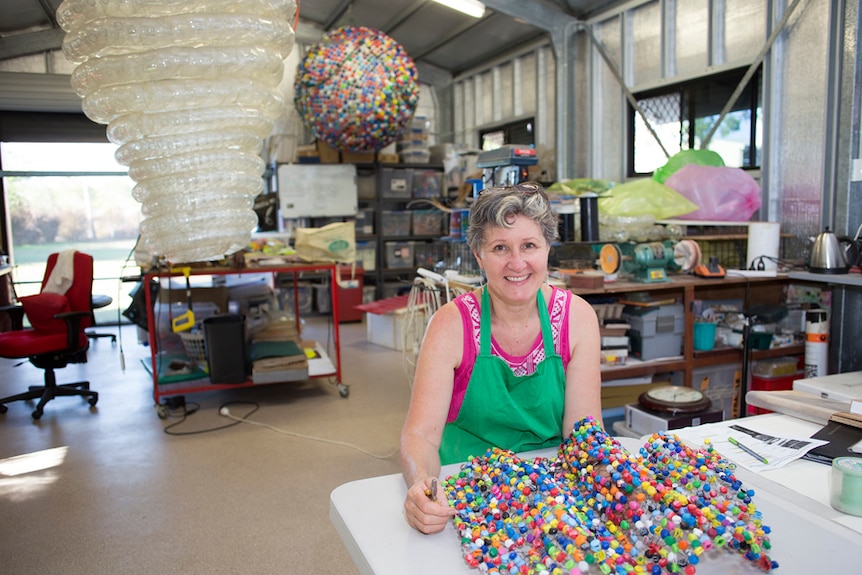 Woman sits with artwork of lots of plastic bottle tops.