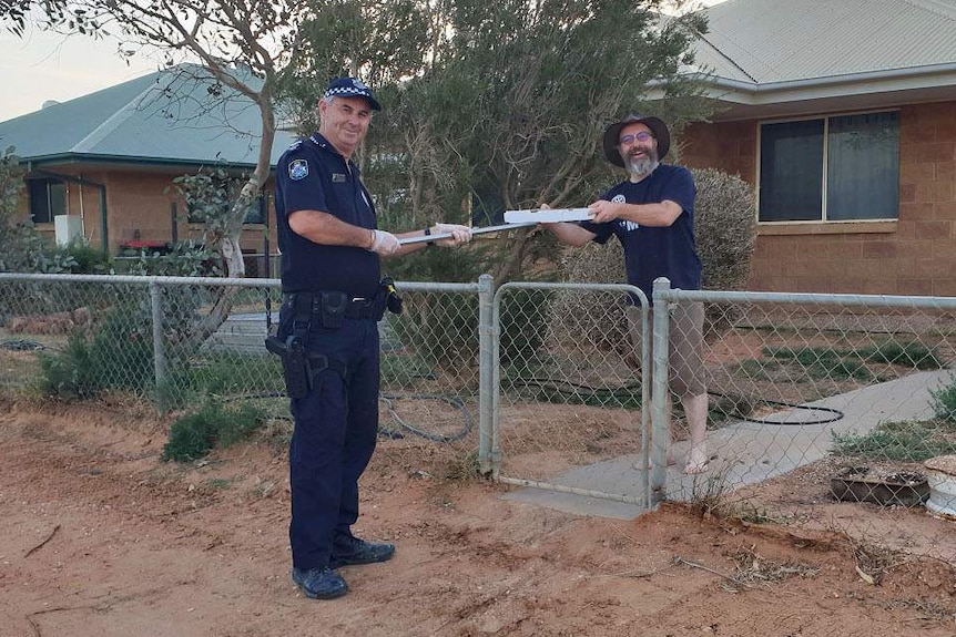 Senior Constable Stephan Pursell use a panhandle to deliver a pizza to a Birdsville resident during coronavirus restrictions.