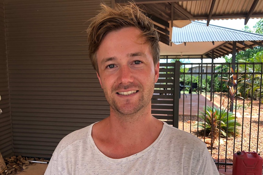 Niall Cooke posing for a photo in a car port with the back yard of a house in the background