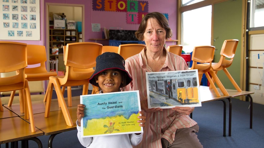 a girl holding a book with an older woman with a book in a school room.