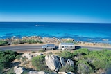 A four-wheel drive tows a caravan on a coastal road with the ocean in the background