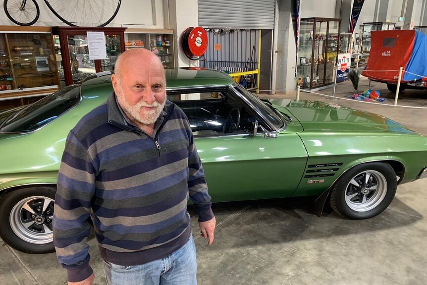 Man standing in front of a green 1970s Holden car in a museum.
