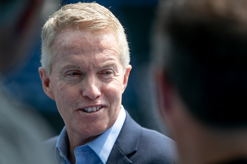 Craig Tiley, dressed in a blue suit, speaks to reporters outdoors.