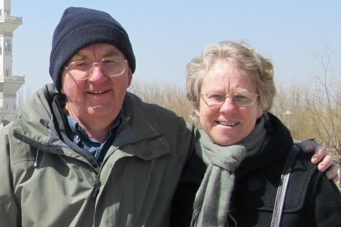 Don and Gail Patterson smile, dressed warmly as they stand under a blue sky outdoors.