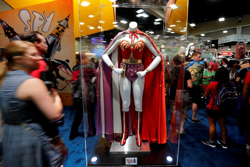 People walk past a Wonder Woman costume in a display cabinet