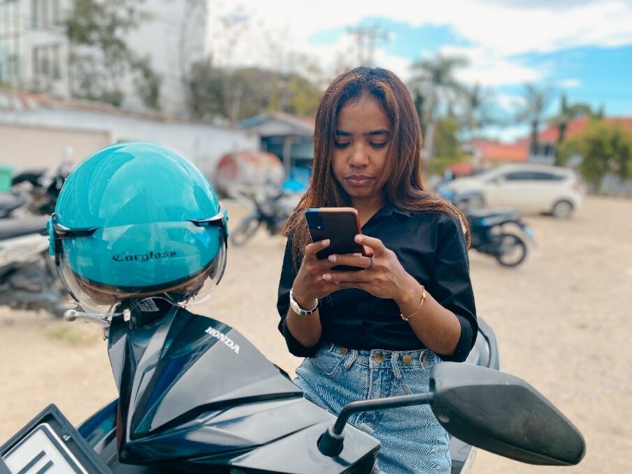 a woman sits on a motorcycle, looking closely at her phone