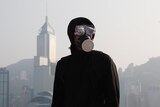 A black-clad protester is pictured in front of the Hong Kong skyline on an overcast day.