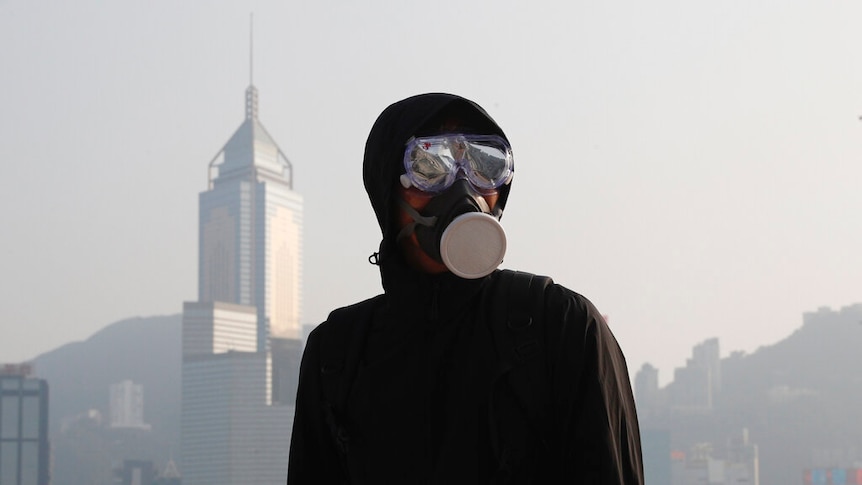 A black-clad protester is pictured in front of the Hong Kong skyline on an overcast day.