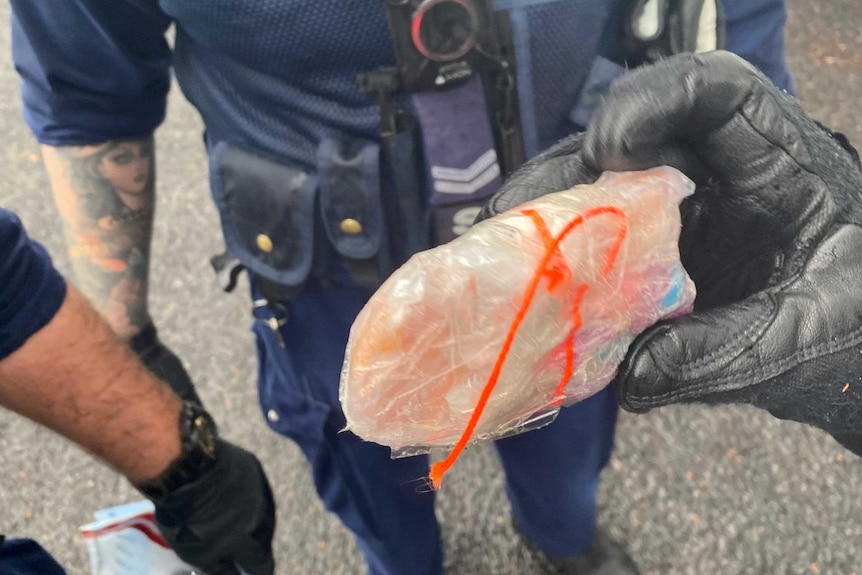 Close up on a package wrapped in plastic being held by policemen.