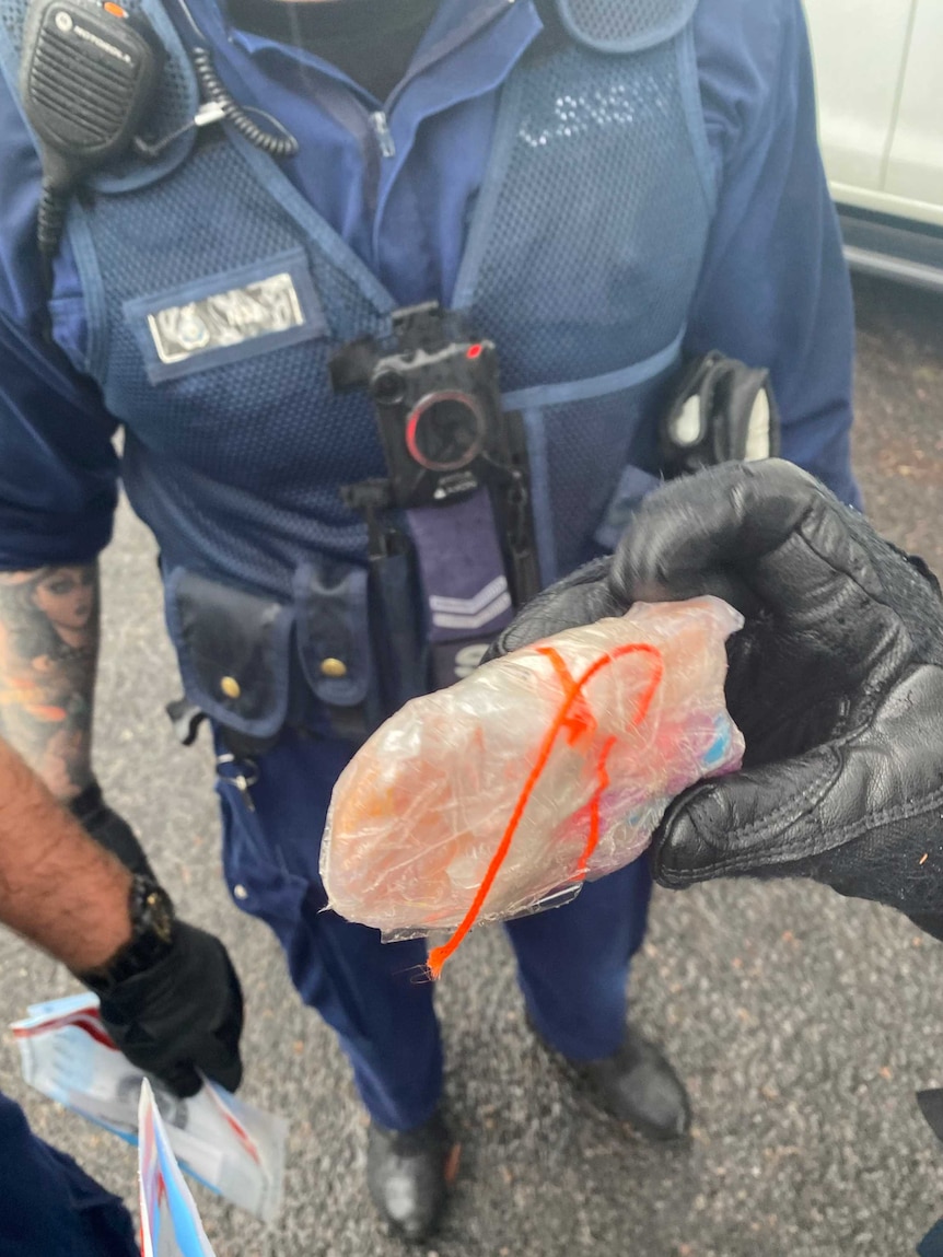 Close up on a package wrapped in plastic being held by policemen.