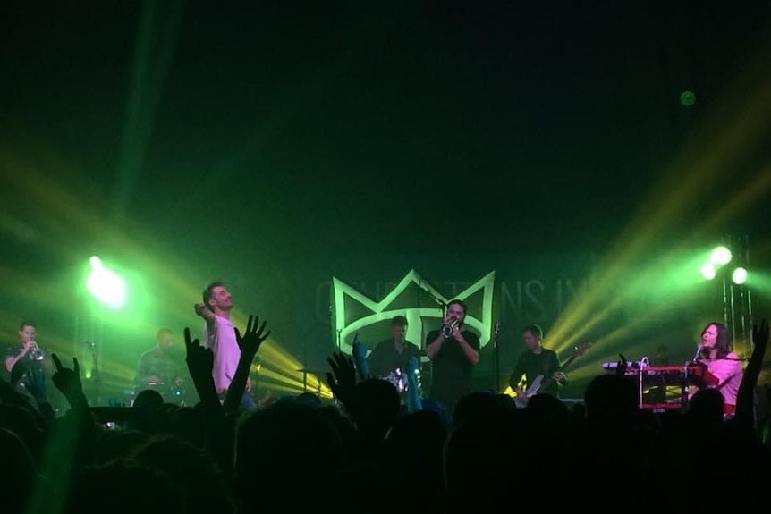 Green light across a stage with a band performing and crowd in front