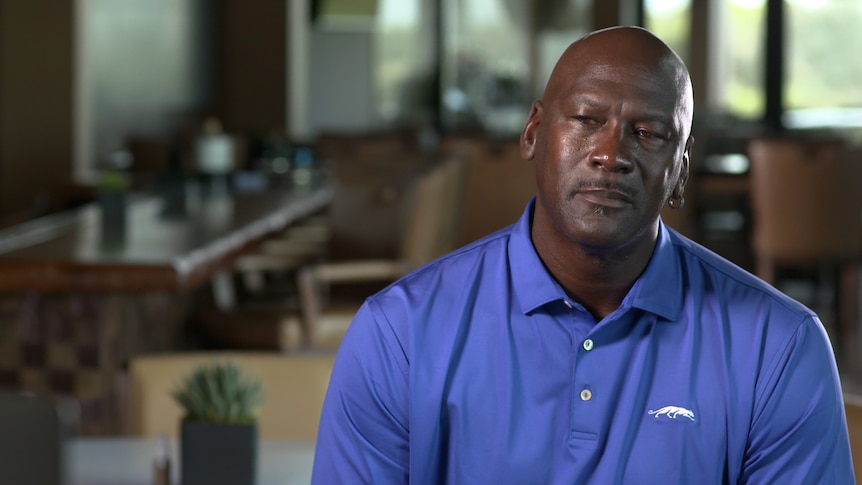 Michael Jordan wears a blue polo shirt seated in interview chair