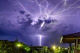 A single bolt of lightning strikes the ground as numerous bolts arc across the night sky, illuminating clouds.