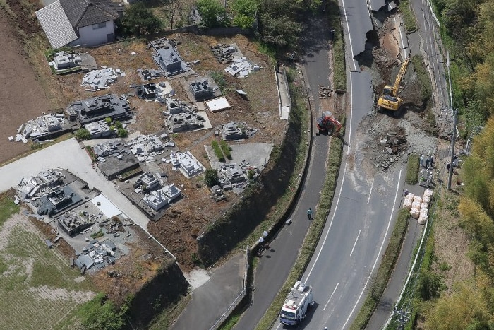 An aerial view showing construction workers restoring a damaged road beside a grave yard.