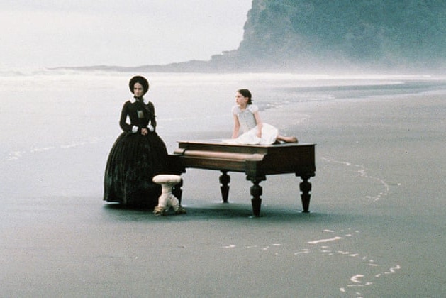 Piano on a beach with two people.