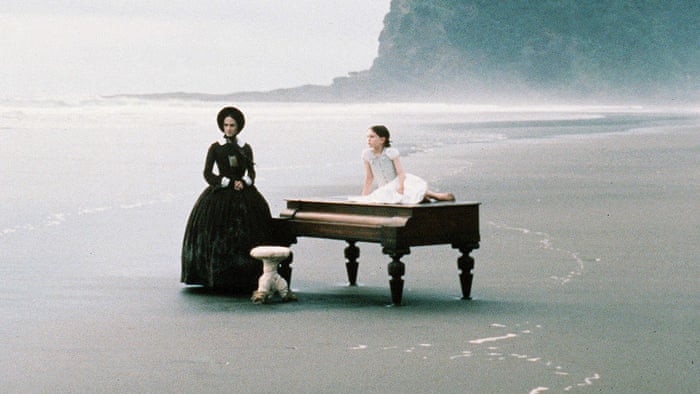 Piano on a beach with two people.