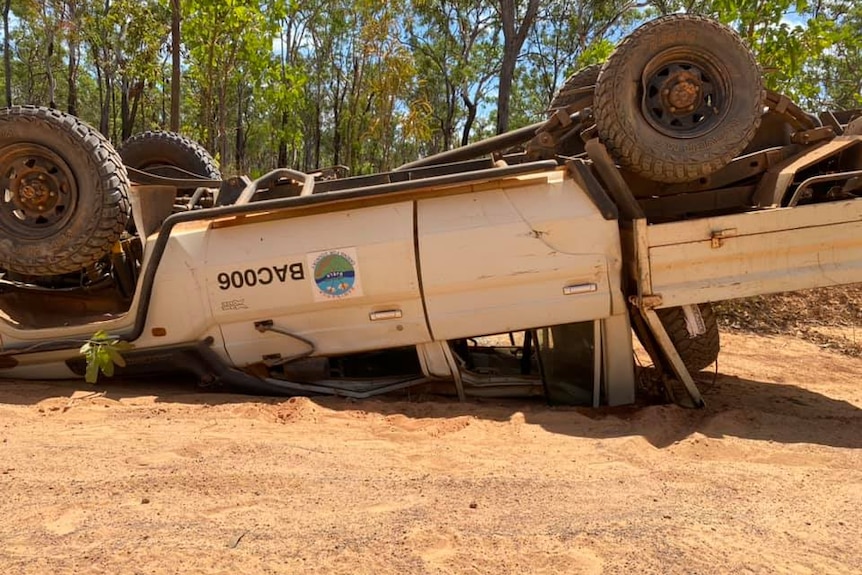 A white Toyota Landcruiser 4WD is seen overturned in sand.