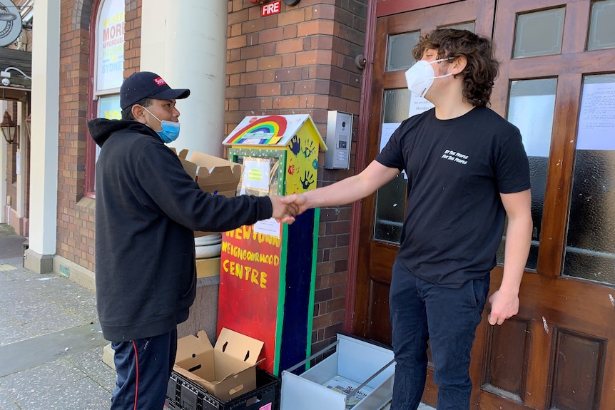 Rhys Bourke shakes hands with a man wearing mask and carrying a box of food.
