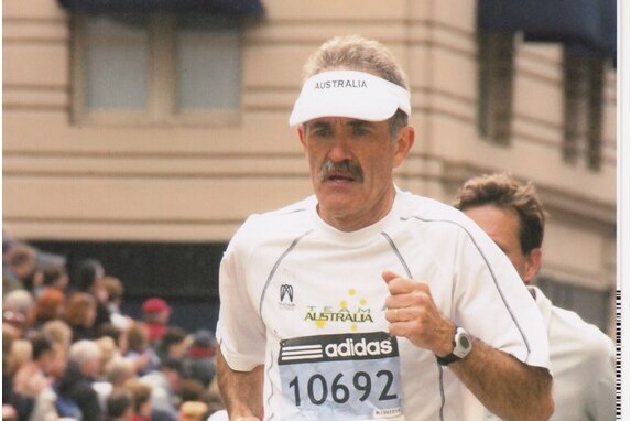 An older man with moustache running a marathon in a city.