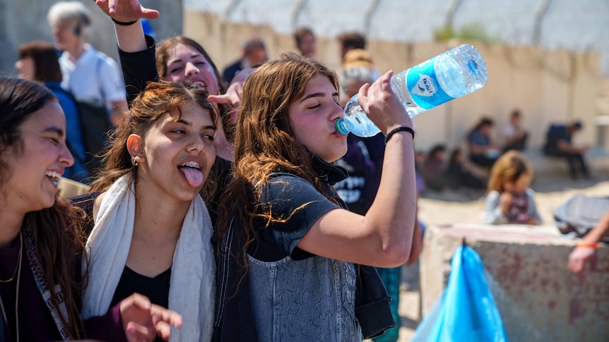 Teenage girls drinking from a water bottle and sticking their tongue out 