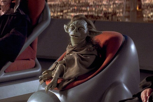 The character of Yaddle sits in a chair in a still from the movie Star Wars: The Phantom Menace
