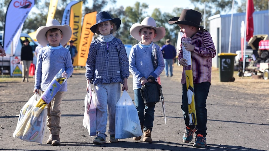 Four young kids dressed in farm attire with akubra's walk towards the camera with showbags