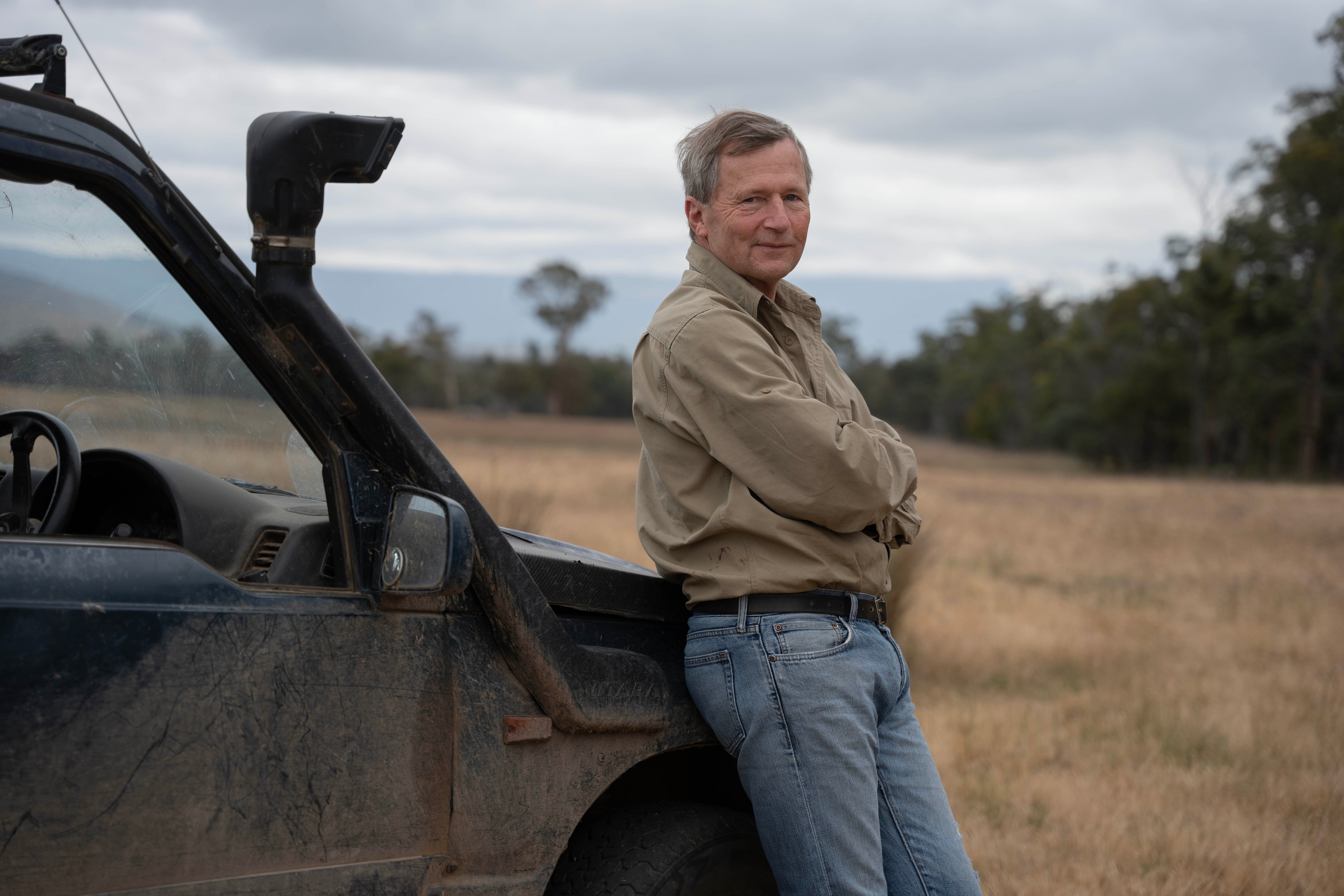 A portrait of a farmer looking at the camera, leaning on a car.