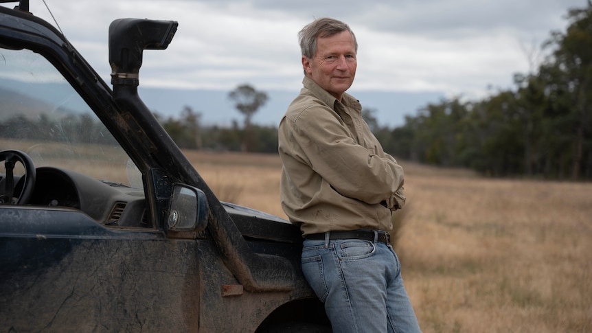 A portrait of a farmer looking at the camera, leaning on a car.