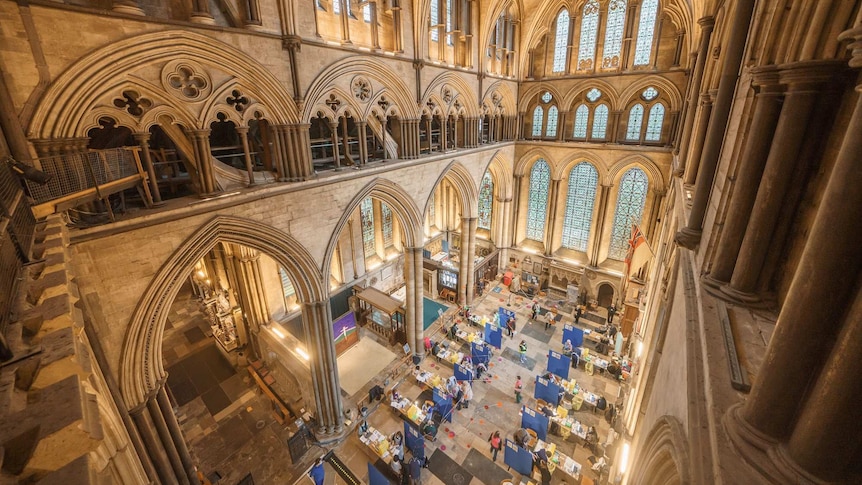 Inside a cathedral with stone walls and stained glass with blue temporary walls and people receiving vaccinations