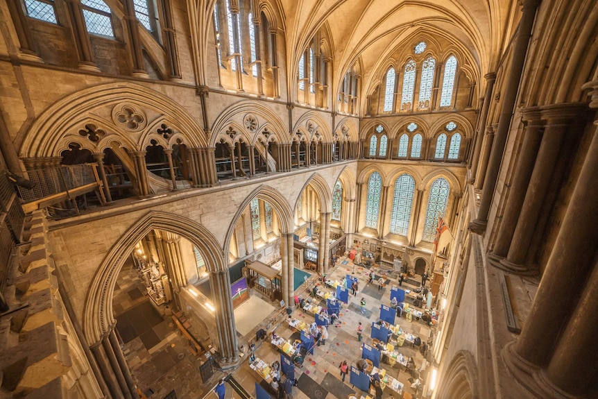 Inside a cathedral with stone walls and stained glass with blue temporary walls and people receiving vaccinations