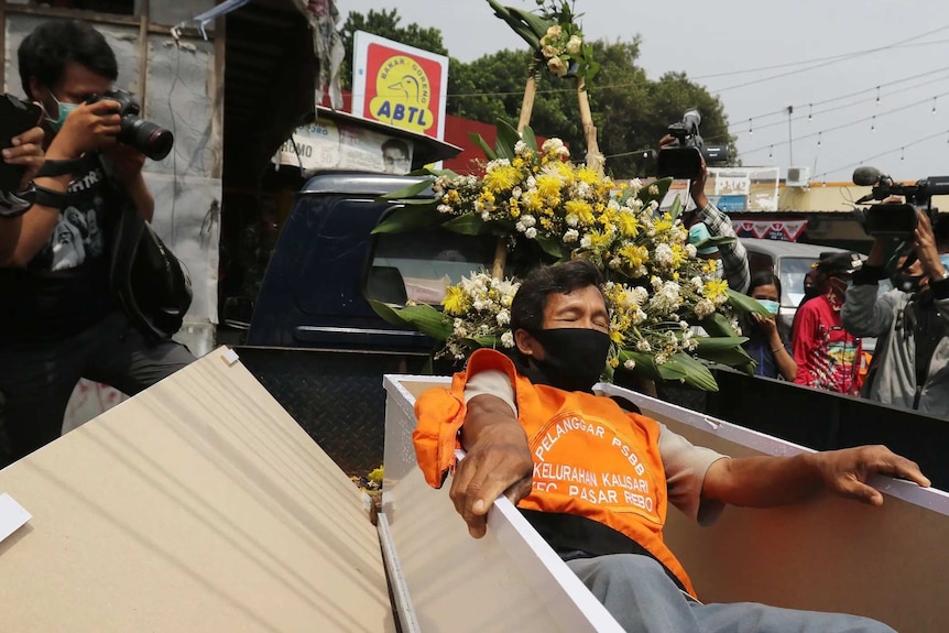 A man is trying to enter a coffin on a street of Jakarta as photographers take pictures.