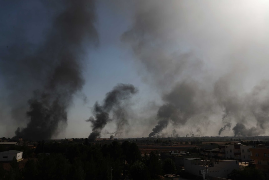 Smoke rises in thick columns in the twilight across the Syrian border.