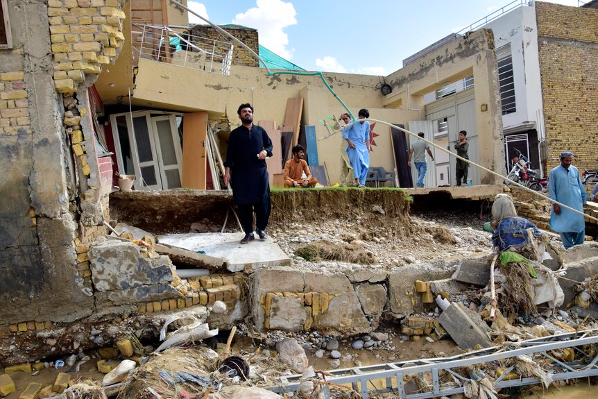 People stand in their partially damage homes caused by flooding after heavy rains.