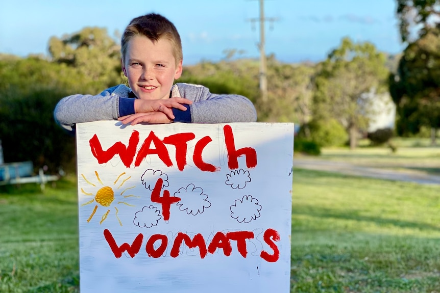 Young boy stands behind his colourful road sign warning of nearby wombats