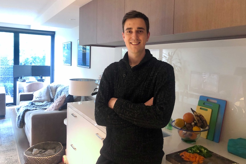 A man wearing a black jumper standing in a kitchen.