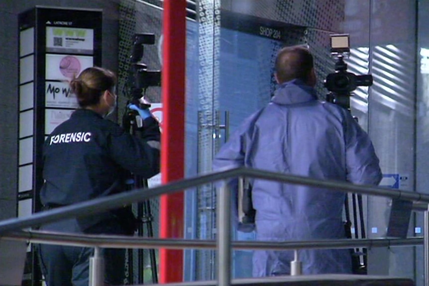 Two forensic specialists hold cameras outside an apartment building.