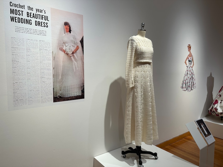 A crochet wedding dress on display on a mannequin next to a clipping from a magazine.
