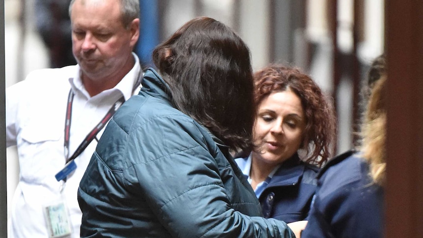 Katia Pyliotis dressed in a blue jacket and black pants is led out of a prison van by prison officers.