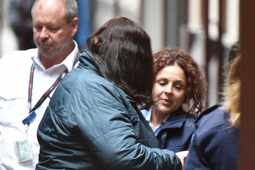 Katia Pyliotis dressed in a blue jacket and black pants is led out of a prison van by prison officers.