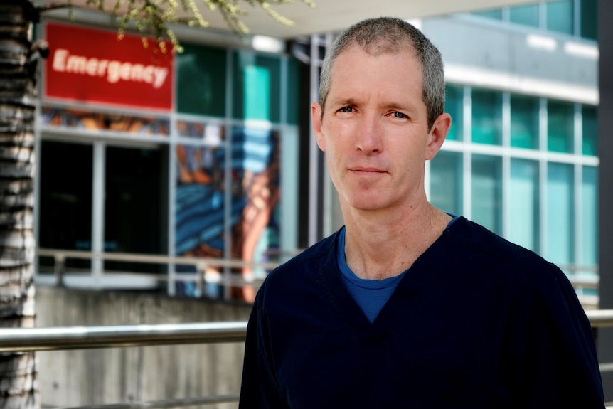 A man stands outside an emergency ward in scrubs.