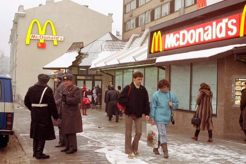 人们在一家红黄品牌快餐店前走过穿着苏式制服的警卫