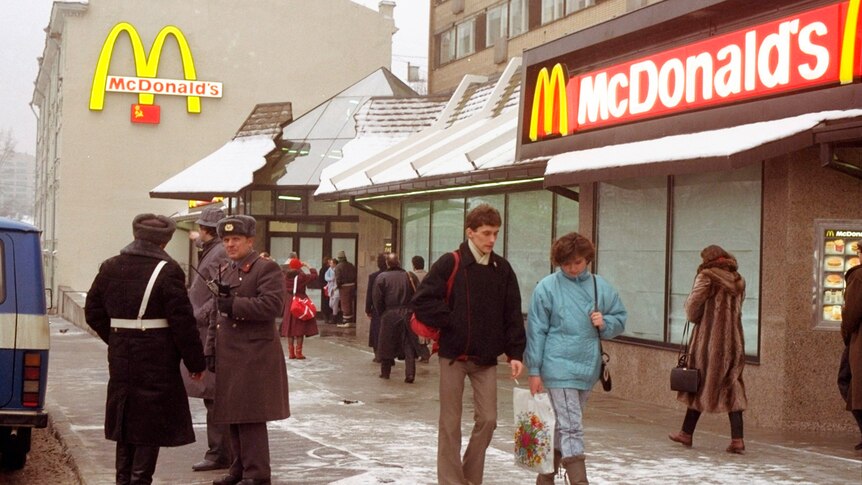 People walk past guards in Soviet-style military garb in front of a fast-food restaurant with red and yellow branding
