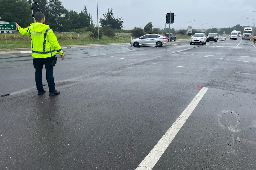 A police officer controlling traffic in the rain.
