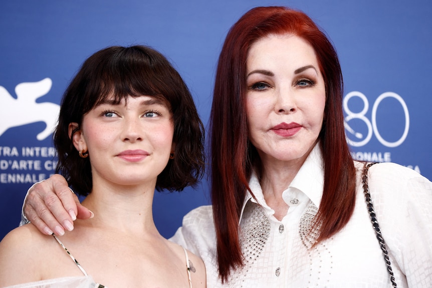 Cailee Spaeny and Priscilla Presley smile together in front of a Venice Film Festival photo wall