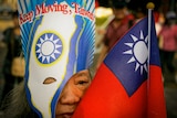 An older Taiwanese woman in a mask with 'Keep Going Taiwan' while her face is obscured by a Taiwanese mask